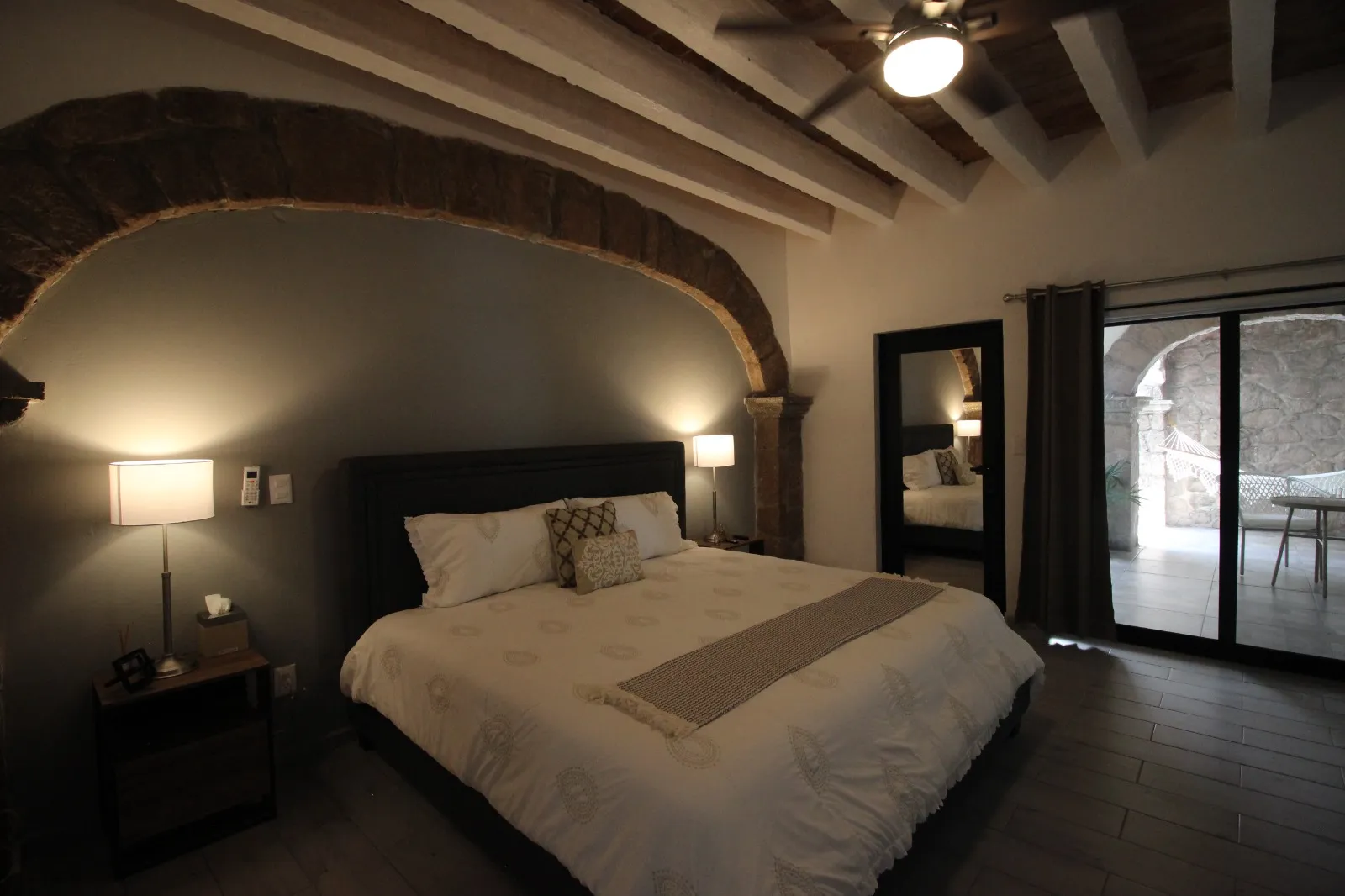 Cama king size bajo arco de piedra, con puerta corrediza hacia el patio con hamaca