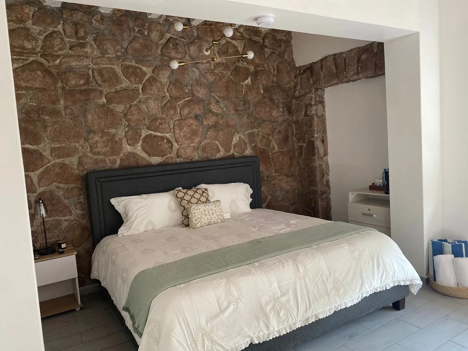 Cama king size bajo pared de piedra con detalles en verde