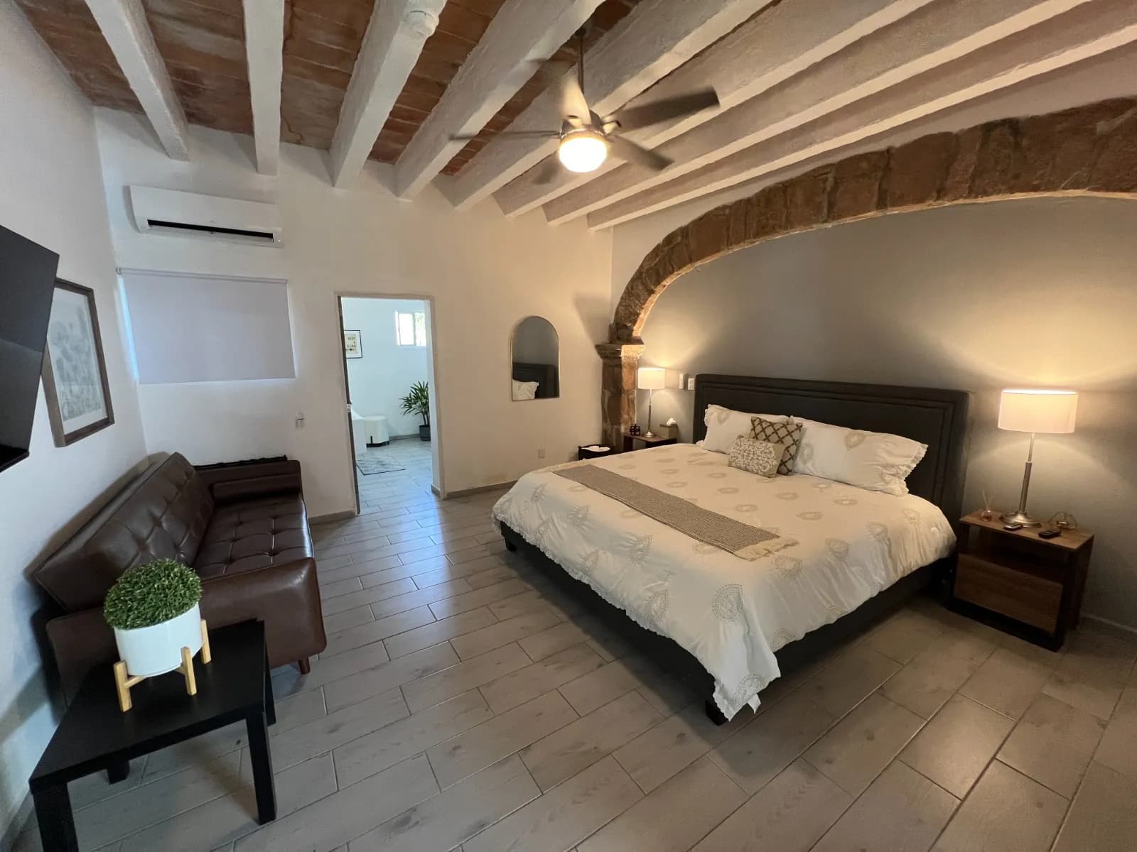 Recámara con cama king size bajo un arco de piedra, sofá de cuero y TV