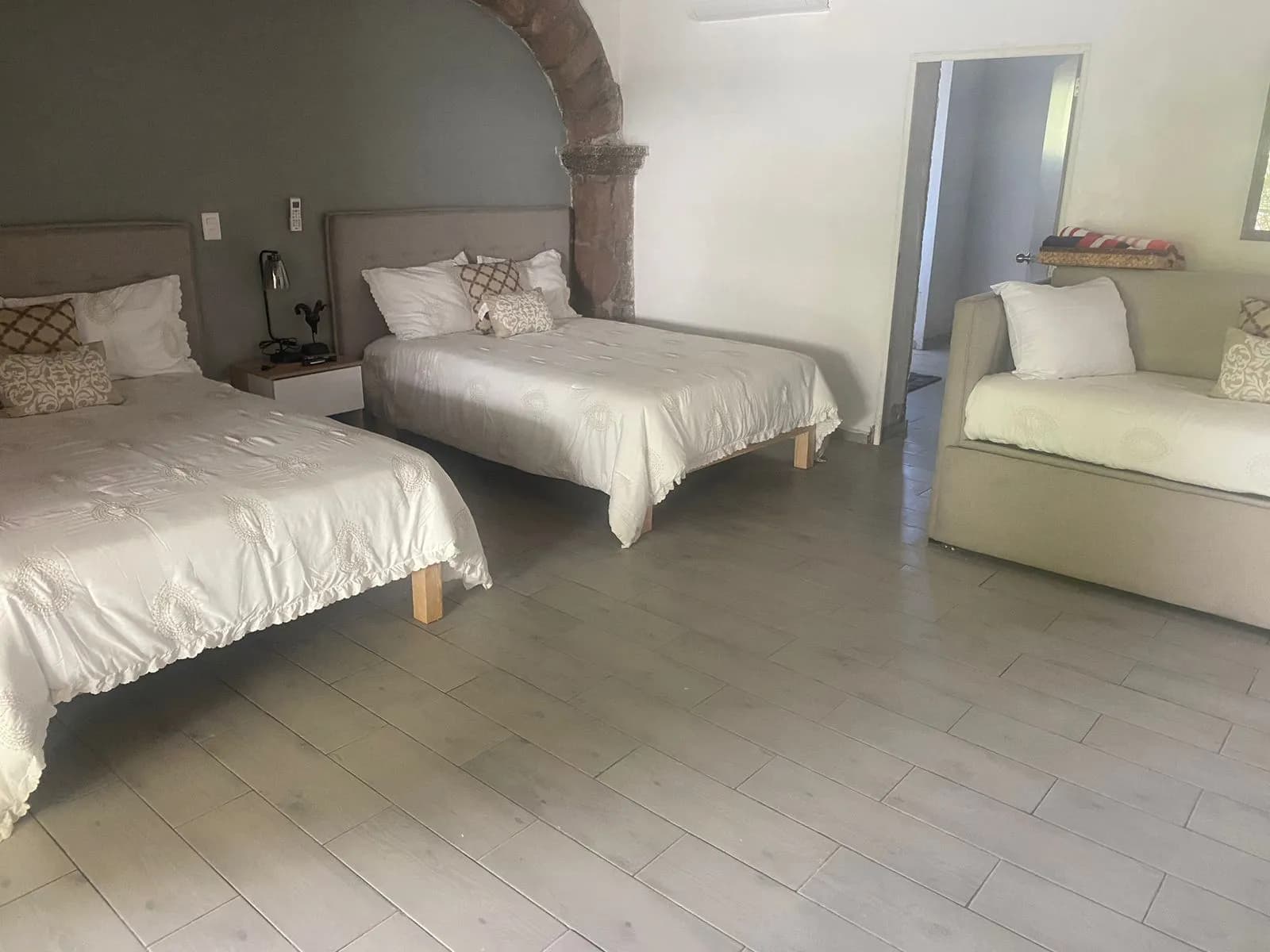 Dos camas matrimoniales bajo un arco de piedra, con sofá cama